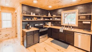 A modern kitchen with dark cabinetry, wooden countertops, and a black backsplash. - Peaceful Hocking Hills Cabin | Hot Tub! Fireplace! (South Bloomingville)