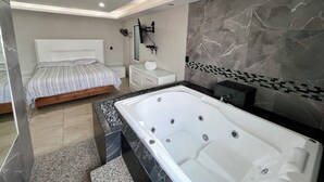 A modern bedroom with a large bed, a separate bathroom with a bathtub, and a vanity with a mirror. - Hotel El Castillo (Cuernavaca)