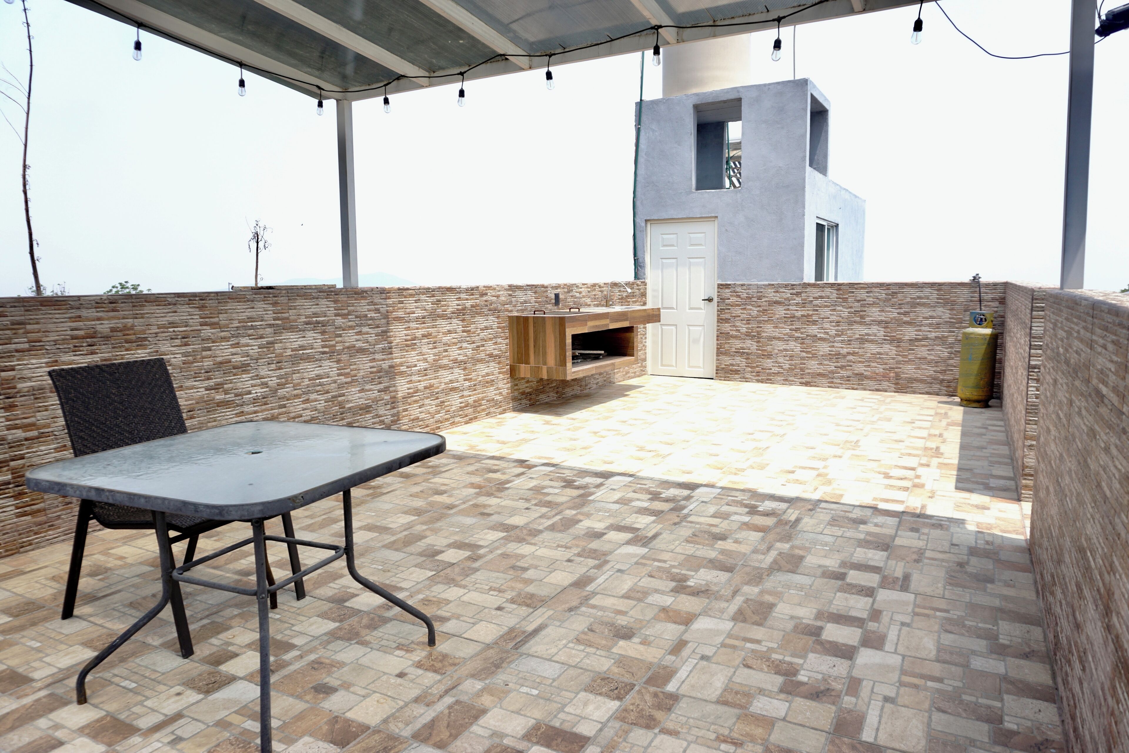 An outdoor patio with a table and chairs, a brick wall, a door, and a small structure with a window.