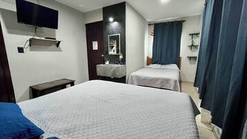 Habitación de hotel con dos camas, un televisor montado en la pared, baño con espejo y cortina de ducha.