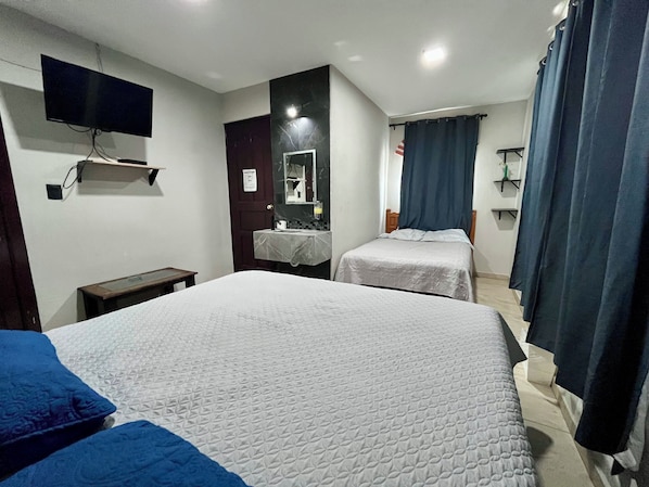 Habitación de hotel con dos camas, un televisor montado en la pared, baño con espejo y cortina de ducha.