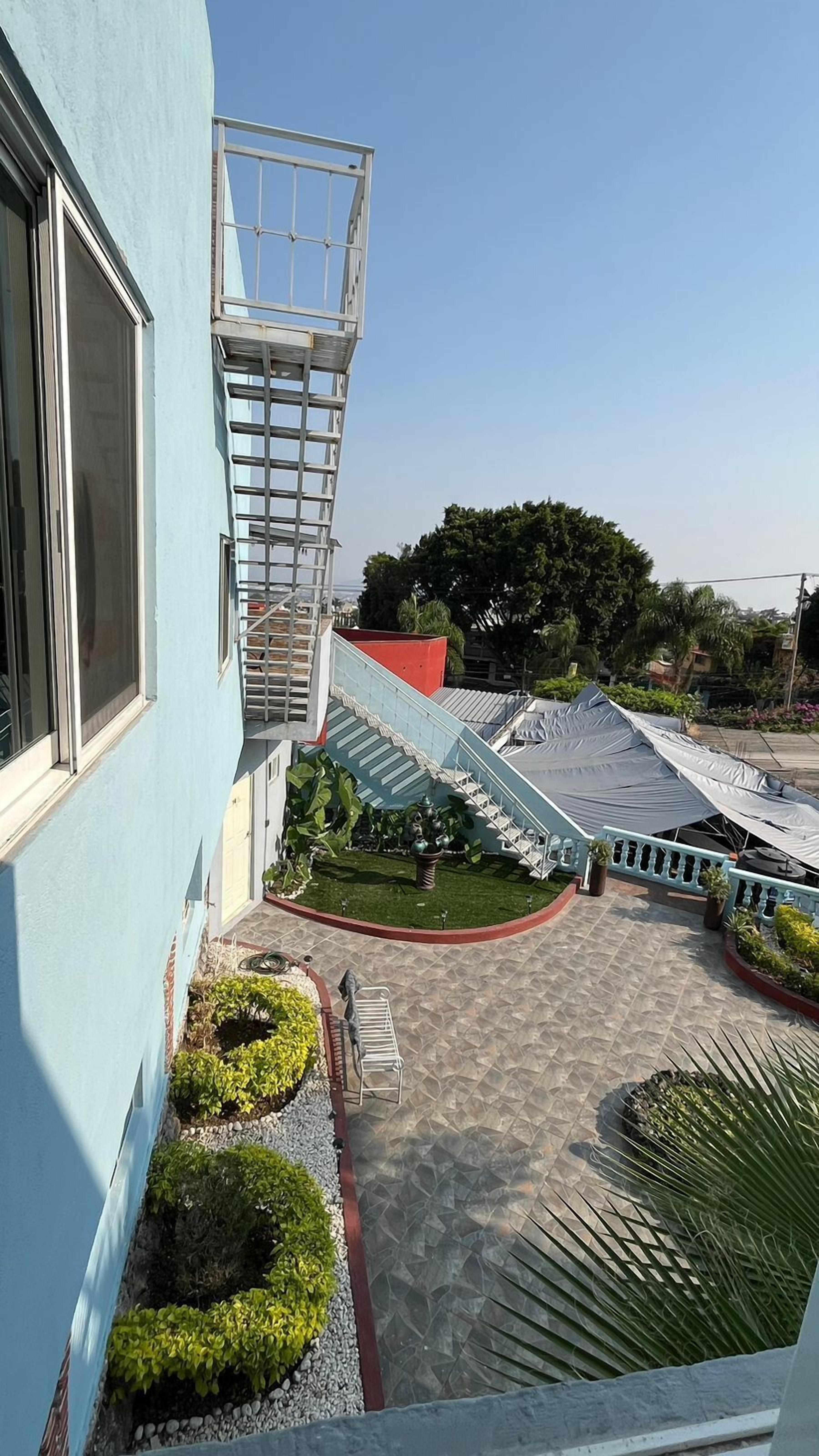 Un edificio con fachada azul, una escalera y un patio con plantas y un banco.