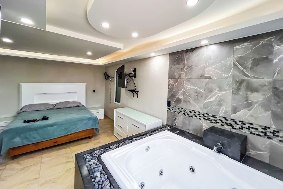 A modern bedroom with a large bed, a separate bathroom with a bathtub, and a vanity.