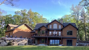 A two-story house with a stone foundation, a balcony, and a large garage. - NEW BUILD! Mountain views, minutes from Squam's Sandwich Beach and boat ramp!  (Center Sandwich)