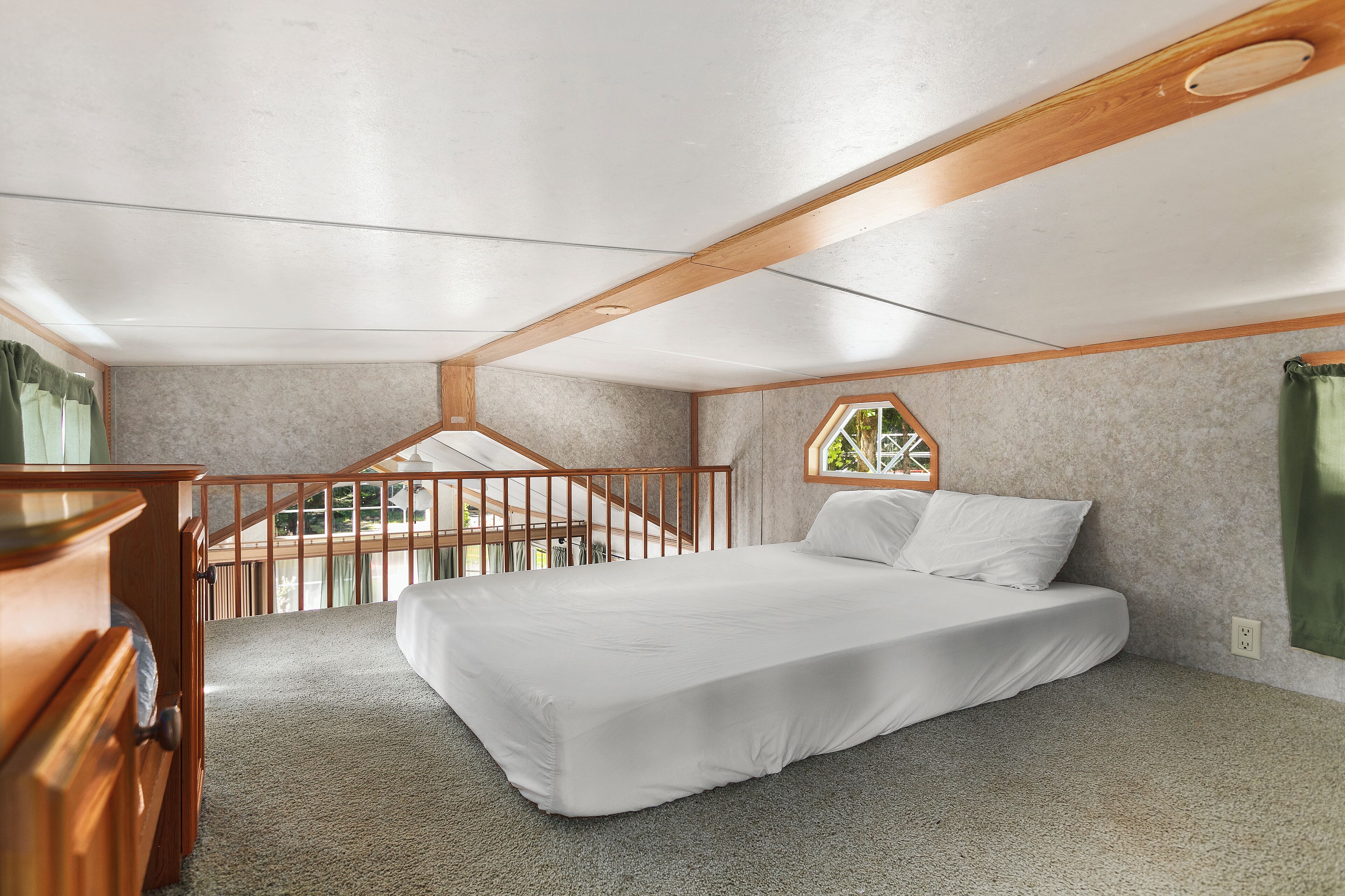A bedroom with a bed, a wooden dresser, a window, and a balcony.