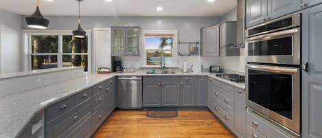 A modern kitchen with grey cabinets, stainless steel appliances, and a wooden floor.