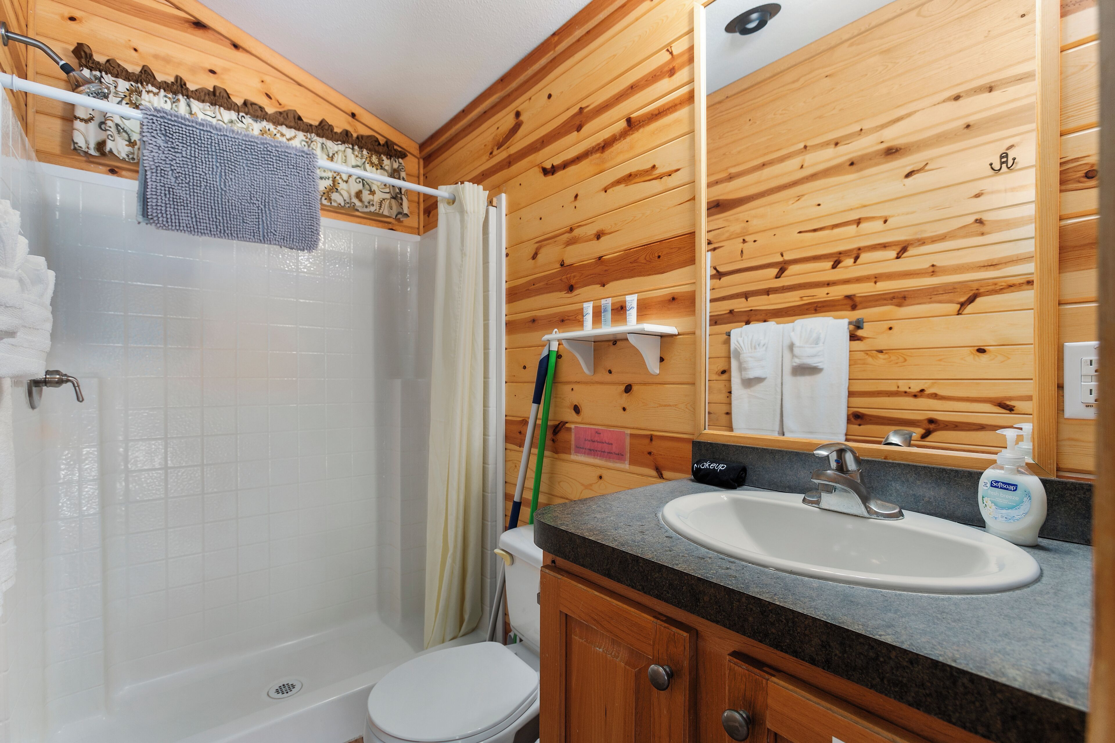 A wooden-paneled bathroom with a shower, toilet, and sink.