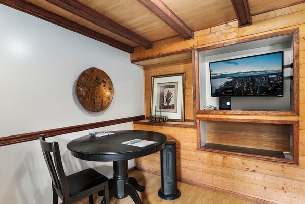 A room with a round table, two chairs, a wall-mounted TV, and a framed picture.