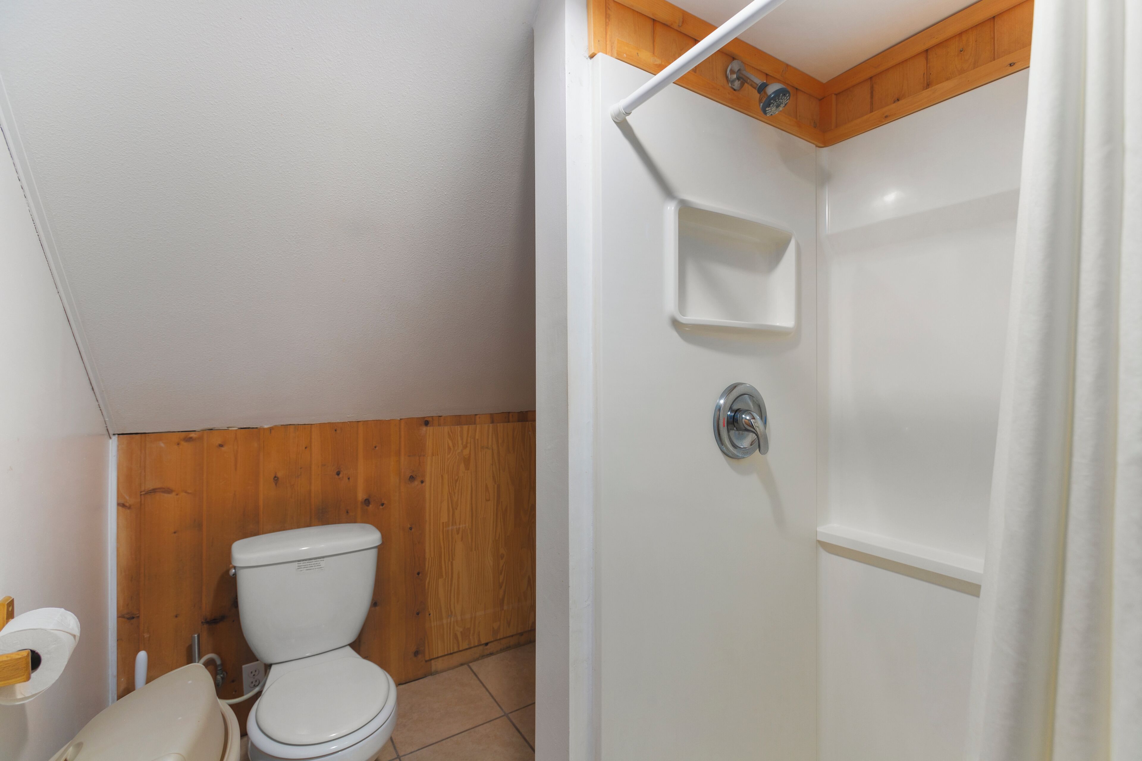 Ein Badezimmer mit Toilette, Holzvertäfelung, einer Dusche und einer weißen Tür.