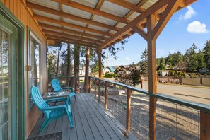 A wooden deck with two blue chairs and a table, overlooking a road and trees. - Robinhood Village Resort (Union)