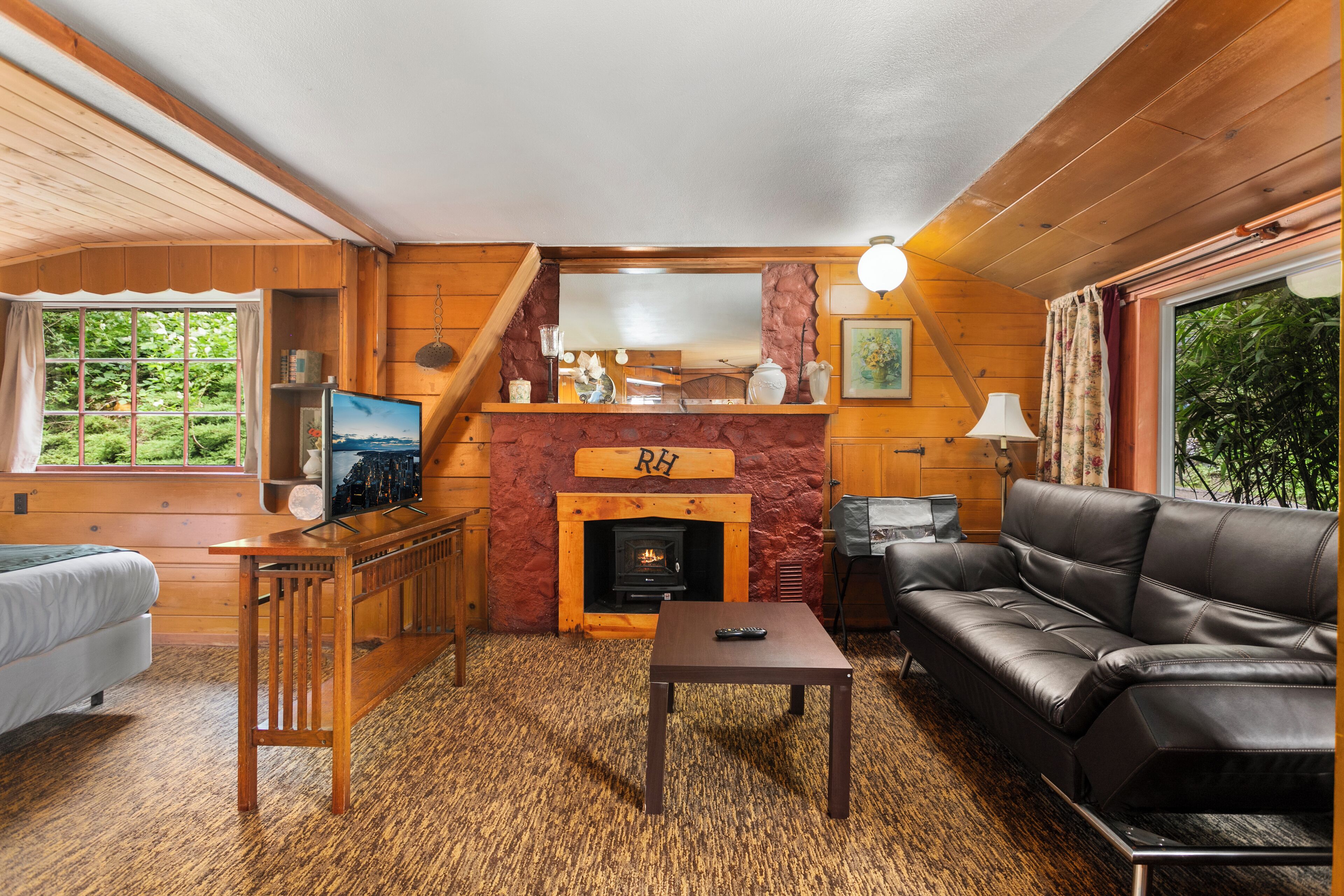 A cozy cabin interior with a fireplace, wooden furniture, a sofa, and a television.