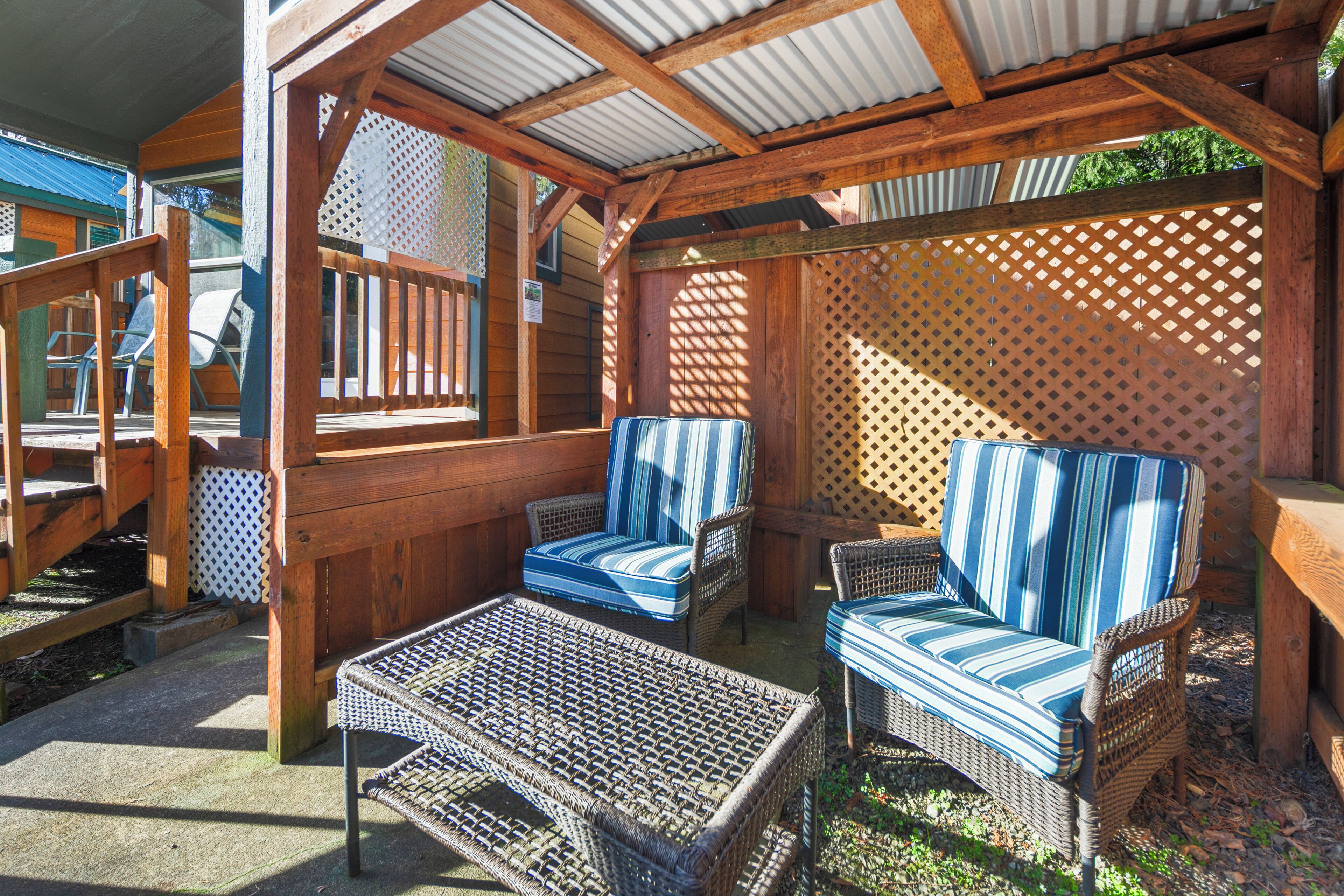 Een overdekt terras met rieten meubels en een houten pergola.
