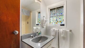 A bathroom with a granite sink, a mirror, a window with stained glass, and white towels hanging on the wall.