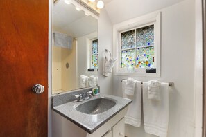A bathroom with a granite sink, a mirror, a window with stained glass, and white towels hanging on the wall. - Robinhood Village Resort (Union)