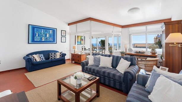 A spacious living room with a blue sofa, a striped sofa, and a coffee table. There is a large window offering a view of the outside.