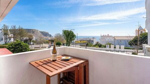 A balcony with a wooden table, a bottle of wine, and a bowl of snacks.