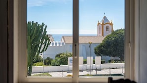 A window view of a building with a white facade and a bell tower, a cactus, and a clear sky.