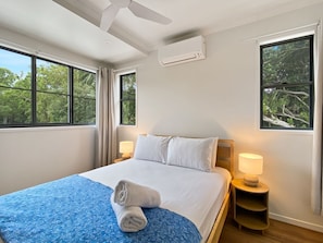 A hotel room with a bed, two bedside lamps, a ceiling fan, and a window with a view of trees. - Picnic Point (Picnic Bay)