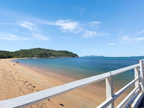 A beach with a wooden walkway, clear water, and a distant forested hill. - Picnic Point (Picnic Bay)