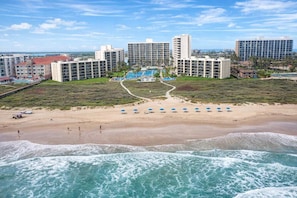 A beachfront hotel with multiple high-rise buildings, a sandy beach with umbrellas, and a view of the ocean. - Saida Towers IV #303 (South Padre Island)