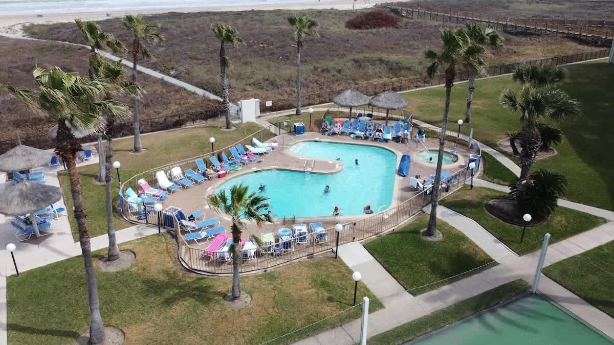 An aerial view of a resort with a large swimming pool surrounded by lounge chairs and palm trees.