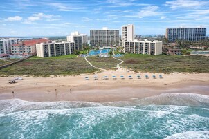 Un hotel frente a la playa con varios edificios altos, una playa arenosa con sombrillas y vistas al océano.