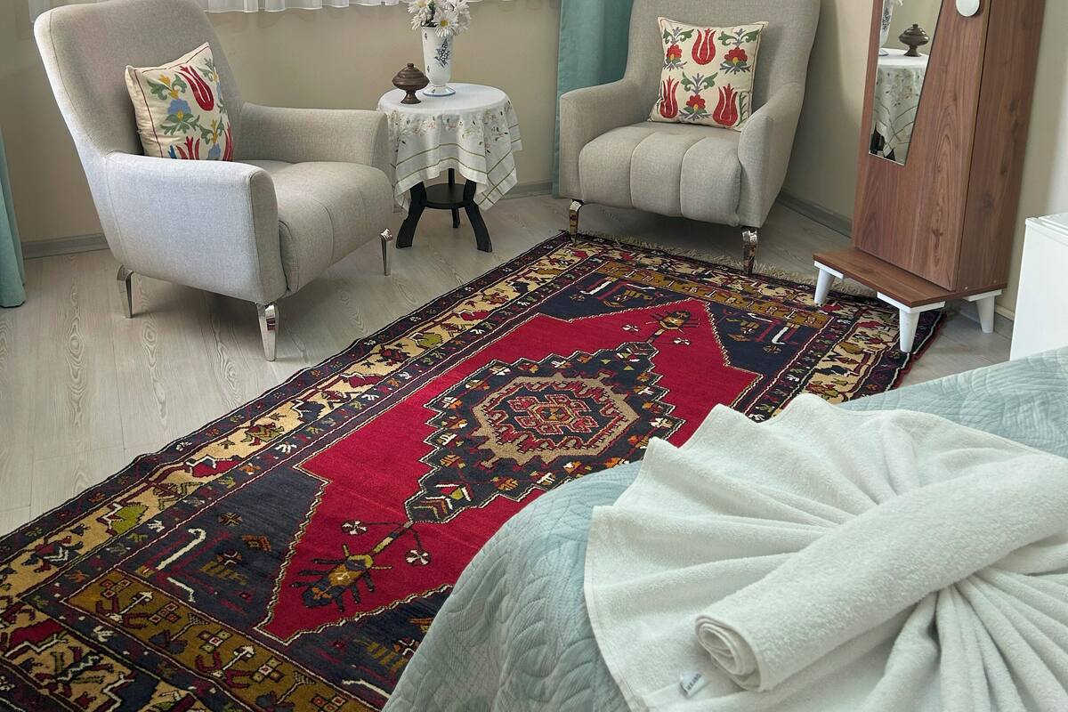 A hotel room with two armchairs, a small round table, a large mirror, and a patterned rug.