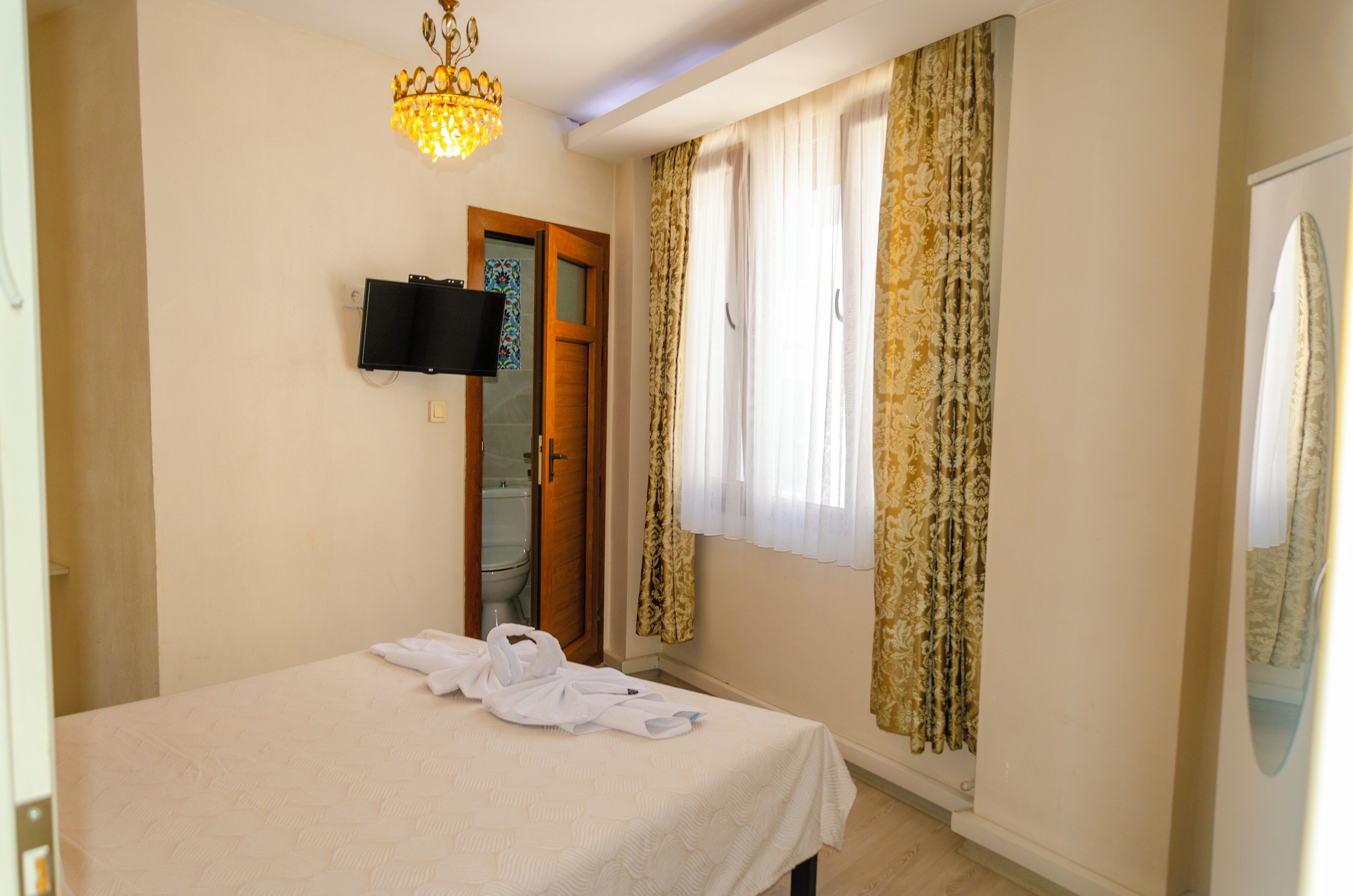 A hotel room with a bed, a television mounted on the wall, a shower, and curtains.