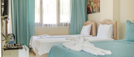 A hotel room with two beds, a TV, a desk, and a window with curtains.