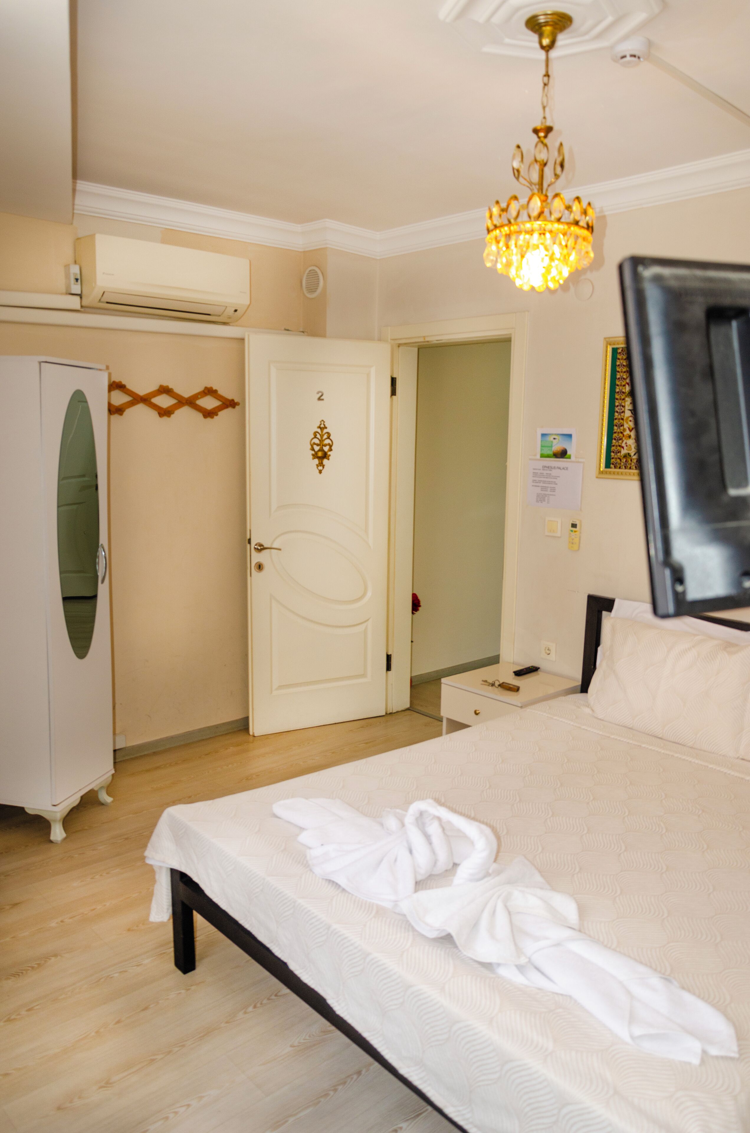 A hotel room with a bed, a TV, a wardrobe, and a chandelier.