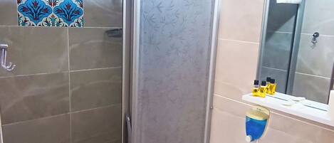A bathroom with a glass shower enclosure, a white sink with a mirror above it, and a tiled wall with a floral pattern.