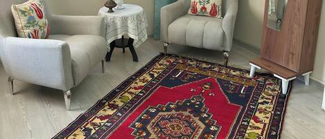A living room with two armchairs, a small round table with a vase, a large mirror, and a patterned rug.