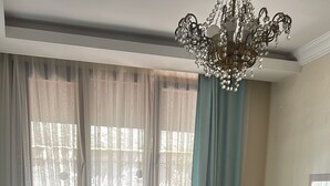 A hotel room with two armchairs, a small round table with a vase, a bed with a quilt, and a chandelier. - Ephesus Palace (Selçuk)
