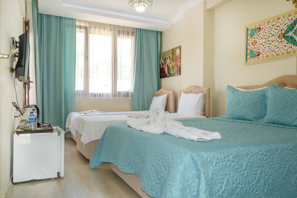 A hotel room with a bed, a small desk with a refrigerator, a television, and a window with curtains.