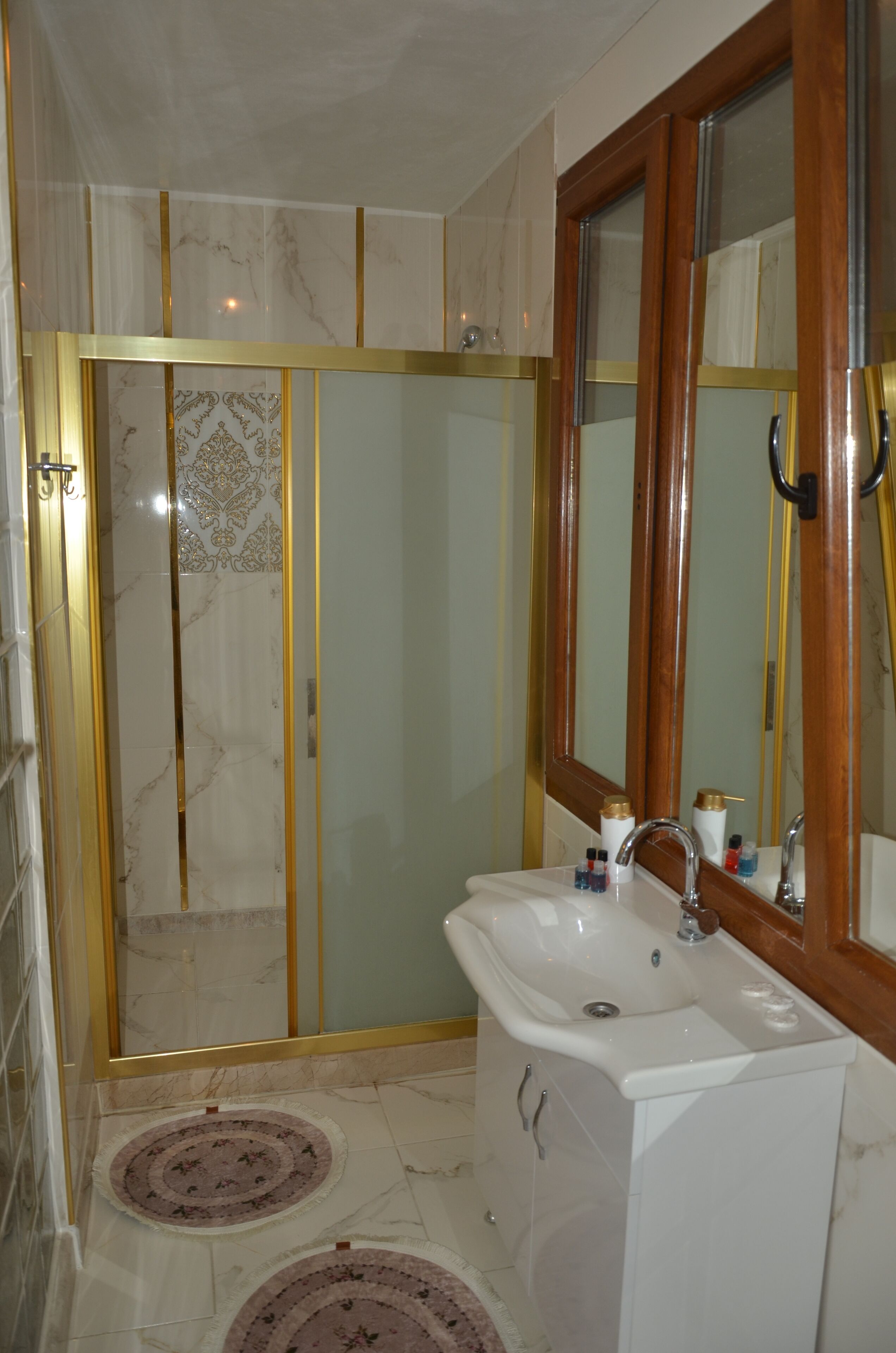 A bathroom with a glass-enclosed shower, a white sink with a mirror, and a tiled floor.