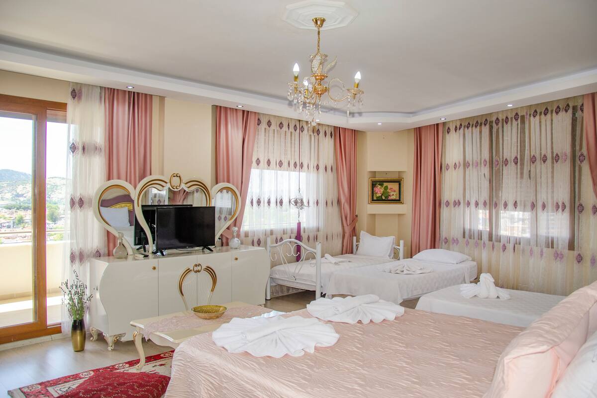 A hotel room with two beds, a TV, a white dresser, and a large window with curtains.