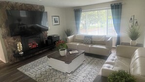 Ein Wohnzimmer mit Kamin, einer Couch, einem Couchtisch und einem großen Fenster mit Vorhängen.