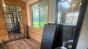 Ein Fitnessraum mit Trainingsgeräten, einem großen Spiegel und einem Fenster mit Blick auf einen Garten.