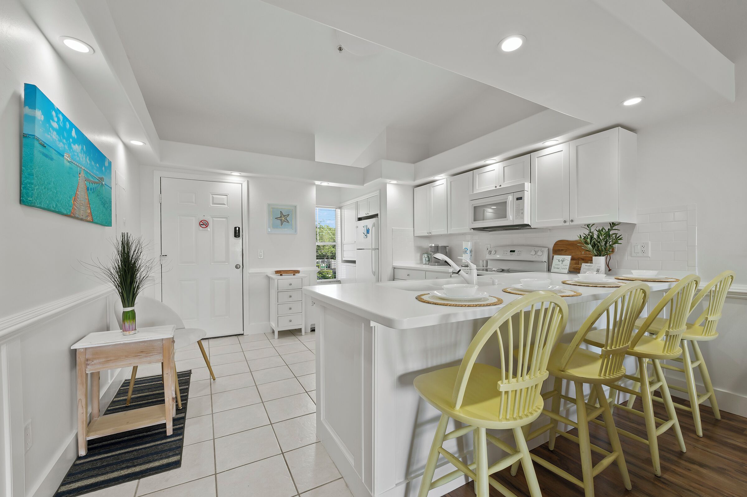 A modern kitchen with white cabinetry, a central island with bar stools, and a view of the outdoors.