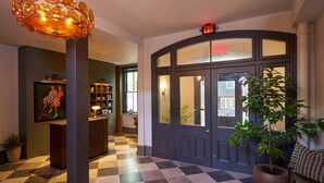 A lobby with a checkered floor, a reception desk, a large potted plant, and a door with an exit sign. - Hotel Anna & Bel (Philadelphia)