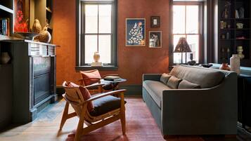 A cozy living room with a fireplace, a sofa, a wooden chair, and a bookshelf.