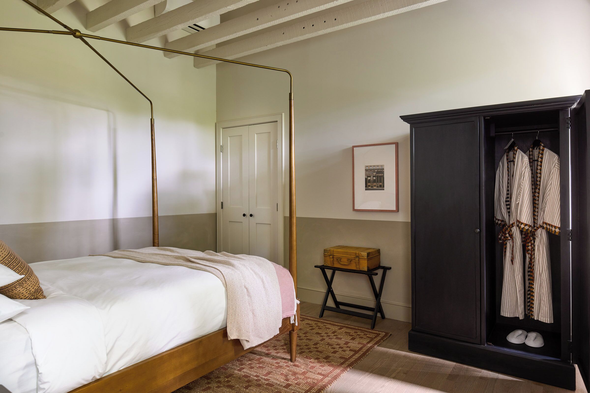 A bedroom with a four-poster bed, a wardrobe, a small table, and a framed picture on the wall.