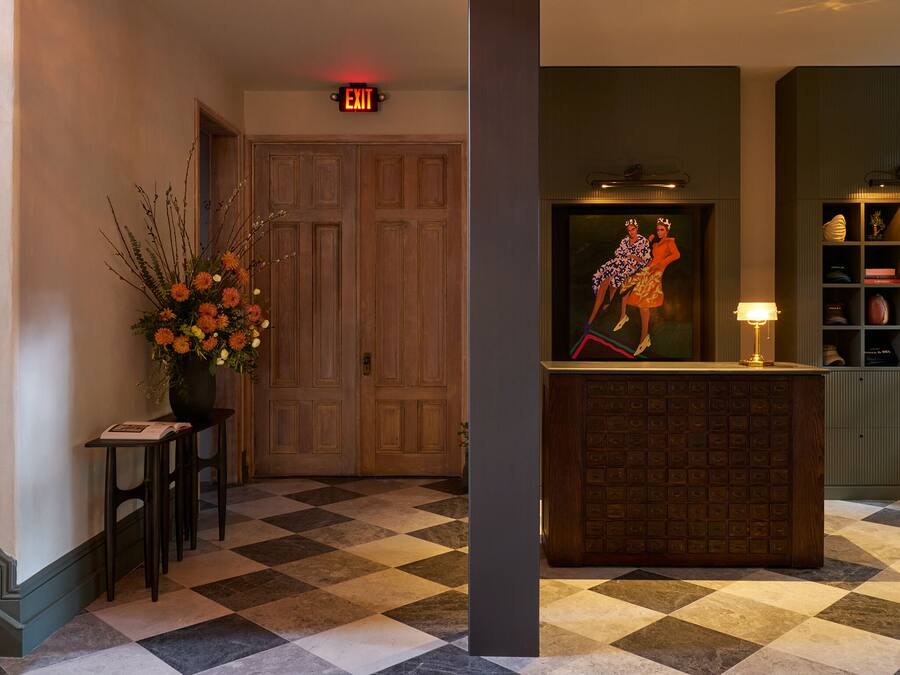 A hotel lobby with a checkered floor, a reception desk, a painting, and a bookshelf.