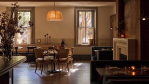 A cozy dining area with wooden furniture, a hanging light fixture, and a fireplace. - Hotel Anna & Bel (Philadelphia)