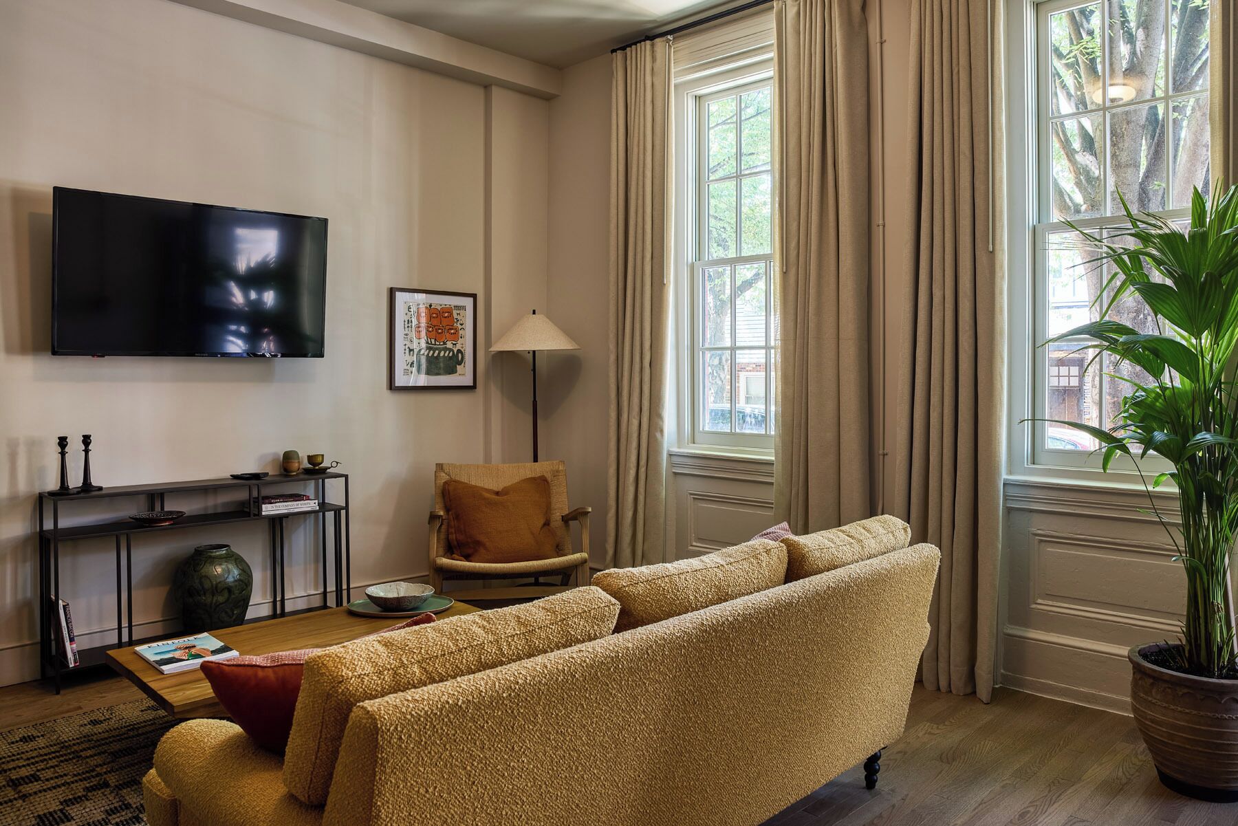 A living room with a sofa, a television, a lamp, a plant, and a window with curtains.