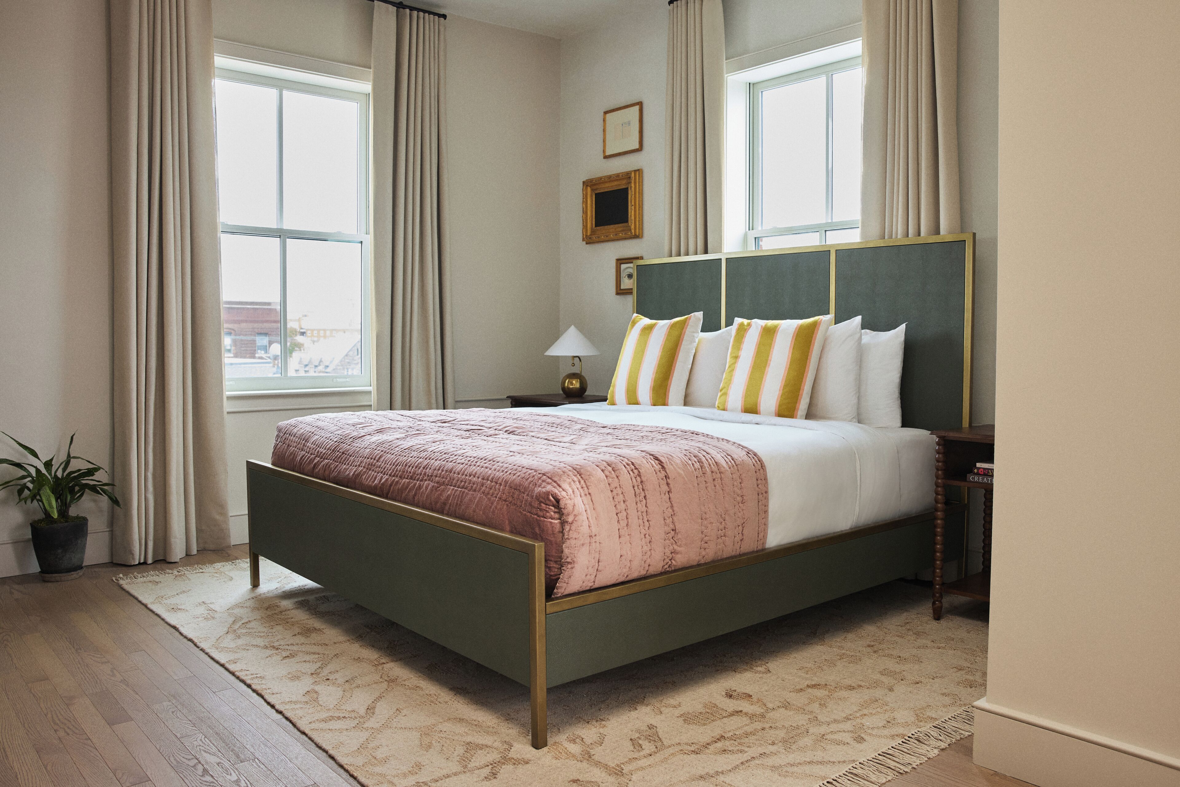 A bedroom with a bed, a nightstand, a lamp, a potted plant, and a window with curtains.
