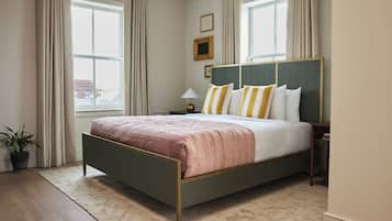 A bedroom with a bed, a nightstand, a lamp, a potted plant, and a window with curtains.