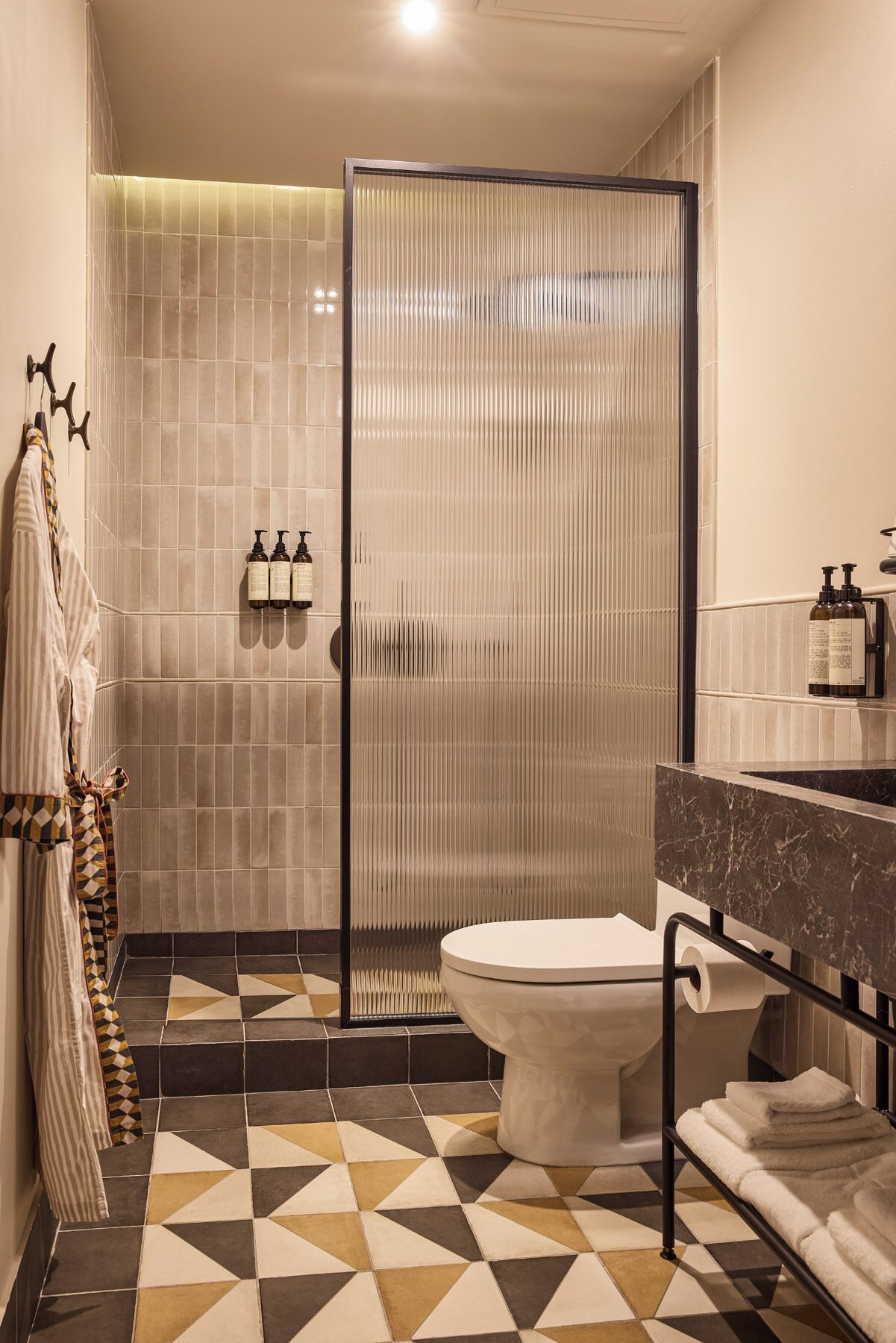 Un baño moderno con cabina de ducha, inodoro, lavabo con encimera de mármol y baldosas de suelo estampadas.