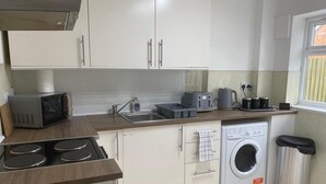 A compact kitchen with a microwave, toaster, sink, and washing machine. - 4BR Sleeps 9 With Garden and Parking (Birmingham)
