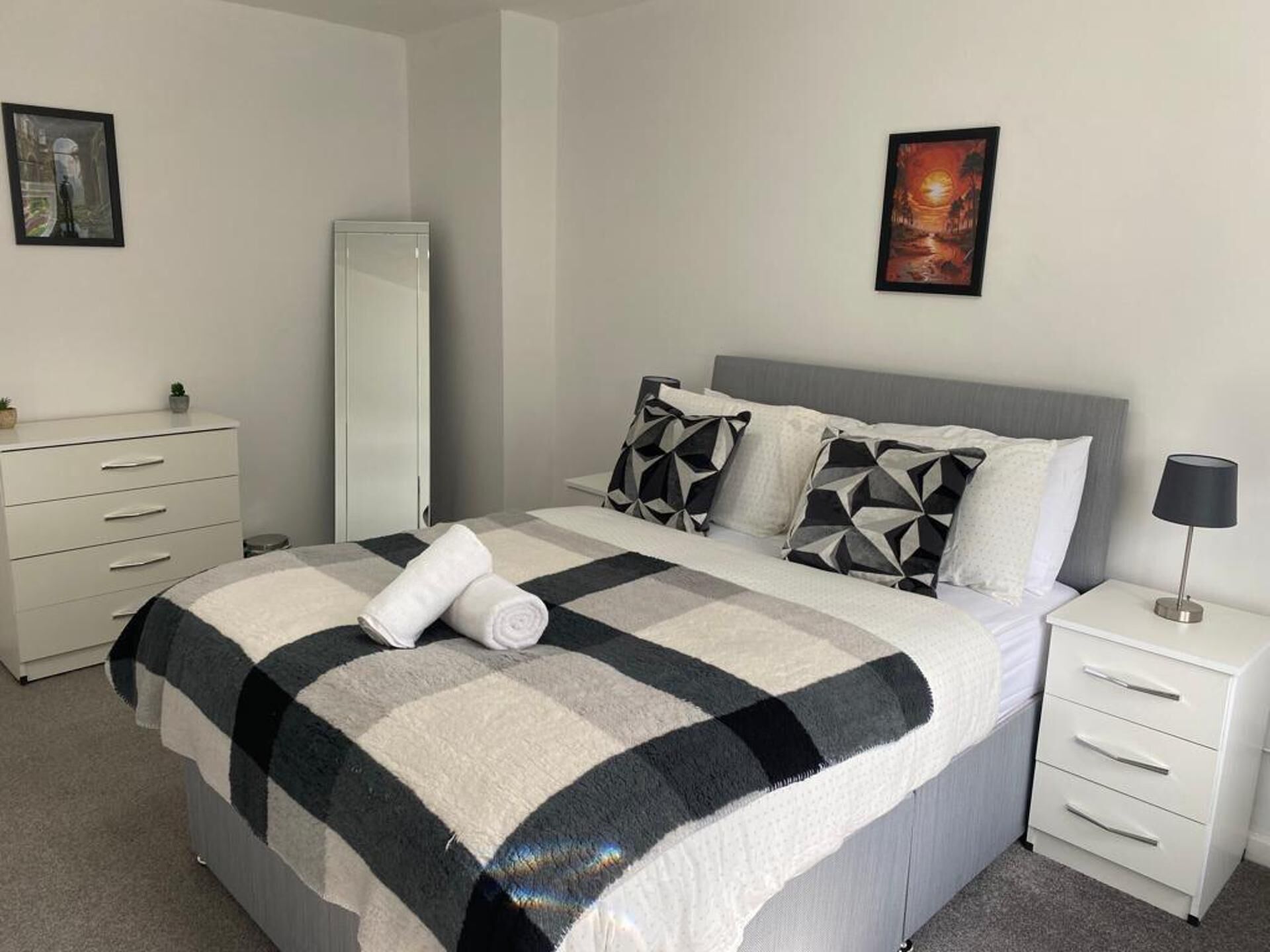 A neatly arranged bedroom with a bed, a dresser, a nightstand, and two framed pictures on the wall.